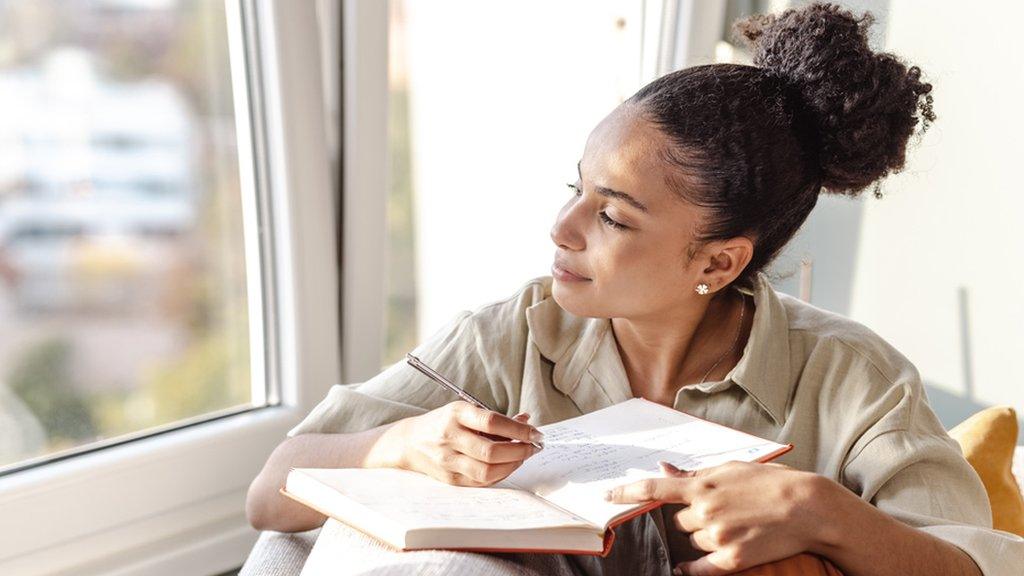 A woman looking out of the window writing a diary