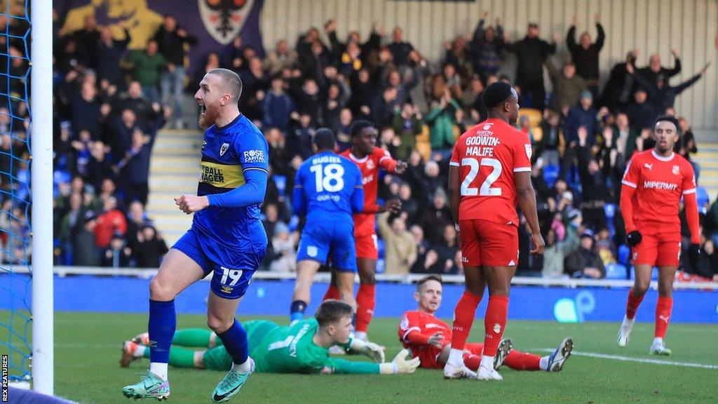 Swindon players (right) look dejected as Wimbledon's Omar Bugiel scores