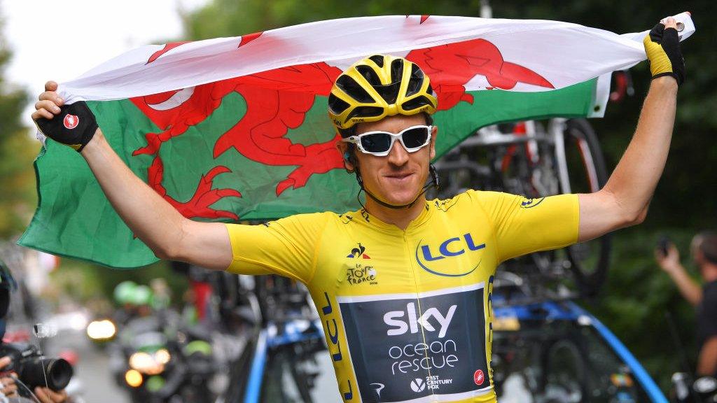 Geraint Thomas holds the Welsh flag aloft as he rides victorious to Paris