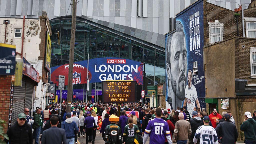 Supporters walk up to Tottenham Hotspur Stadium, which is decorated with NFL branding, and past a Harry Kane mural painted on the side of a building