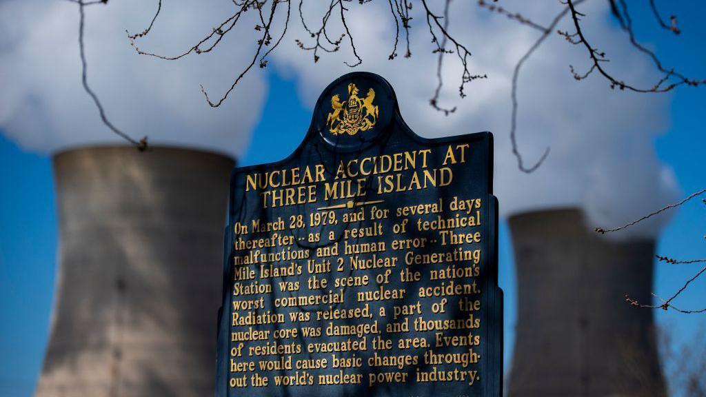 a historical marker remembers the 1979 Three Mile Island nuclear accident while steam rises from cooling towers in the background