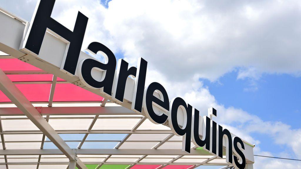 A Harlequins sign on the end of a white roof which has diamonds containing club's colours of green, red and blue