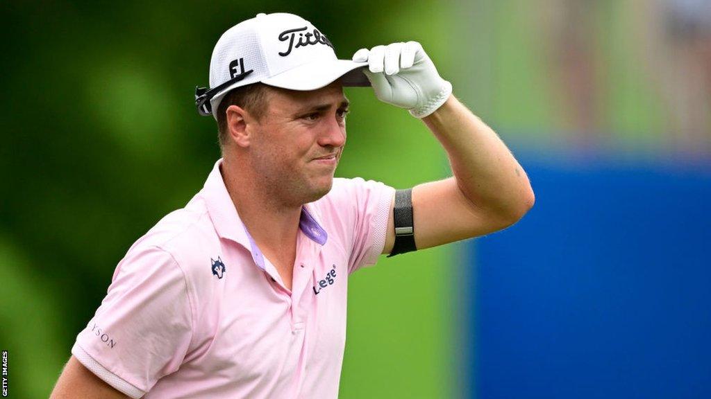 Justin Thomas holds his hand up to his hat