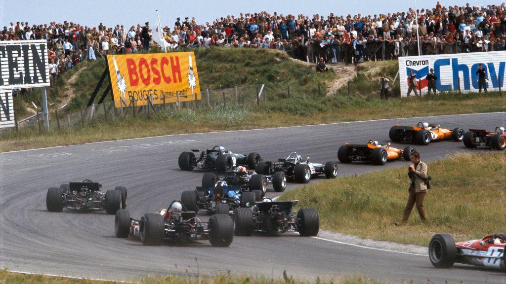 A photographer stood on the inside of the first corner, Tarzan, as cars go round it at the start of the 1969 Dutch Grand Prix