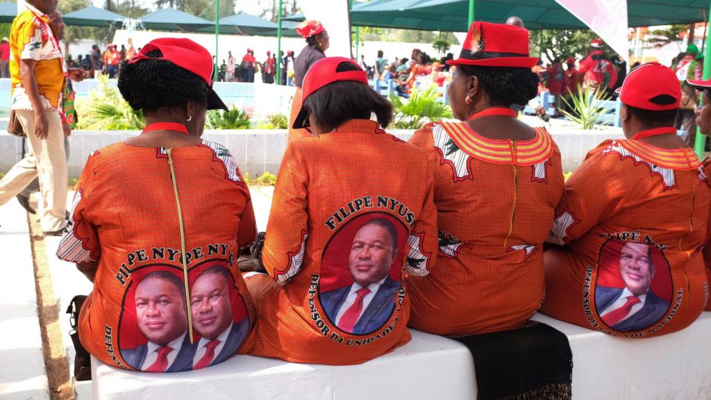 Women sitting in a row with matching dresses praising Filipe Nyusi