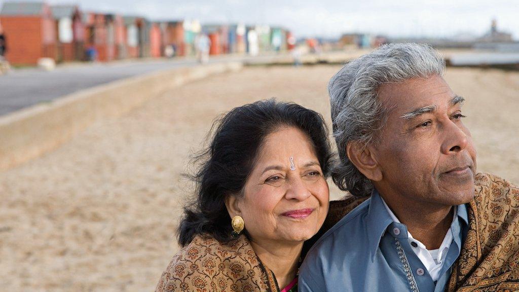 An Asian mature couple look out to the sea as they stand on the beach