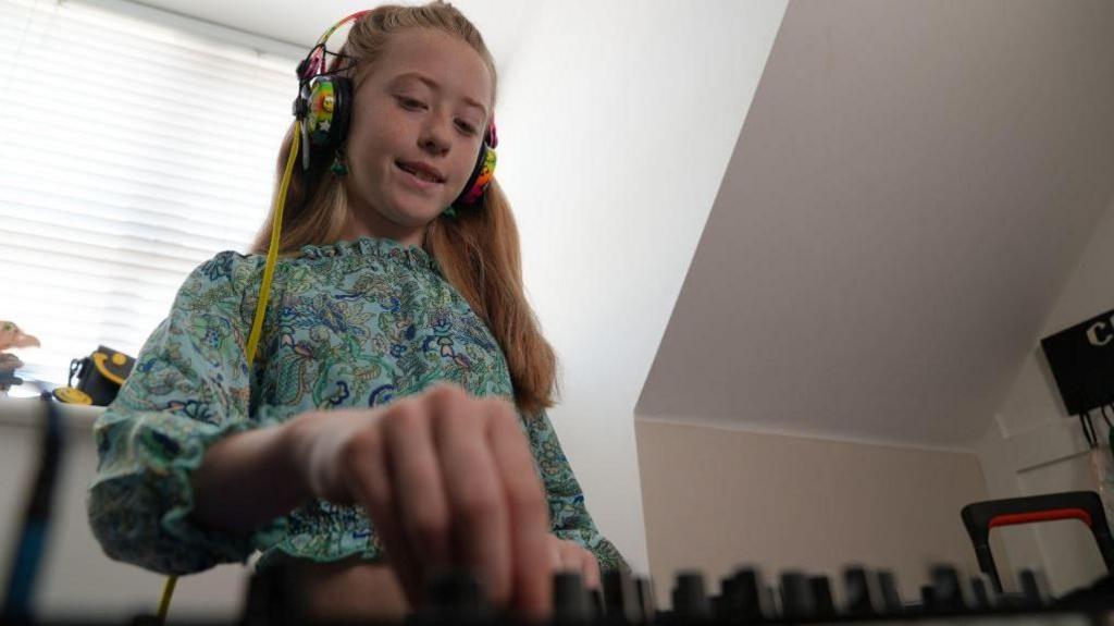 An action shot of a 10-year-old girl with long blonde hair twisting dials on a DJ deck.