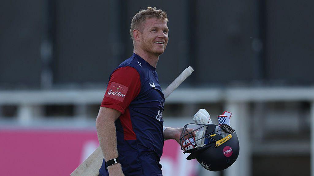 Sam Billings holding his helmet in his left hand with his bat under his arm as he walks off the pitch during a match for Kent