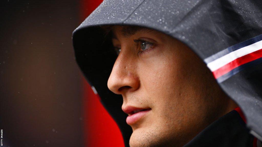 George Russell stands with his hood up amid rain in the Belgian Grand Prix paddock