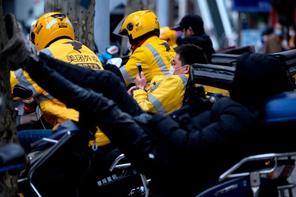 Motorcycle delivery workers wearing protective facemasks wait for orders along a street in Shanghai.