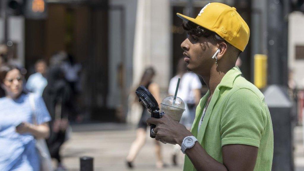 A man stands with an iced drink and a fan