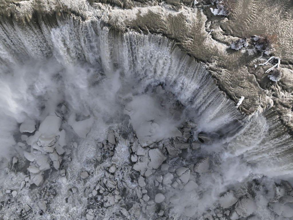 An aerial view of large snow-capped ice chunks at the foot of the falls