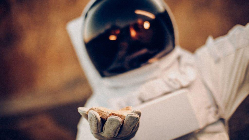 astronaut holding some rock in his hand