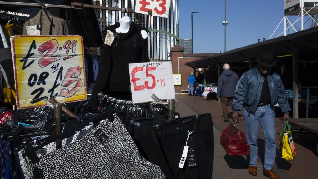 A man carrying two bags walks through the outdoor stalls in Leeds, United Kingdom. 19 March