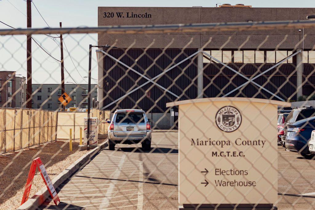 Fence and gate in front of parking lot where a sign says "Maricopa County" and has arrows to elections warehouse