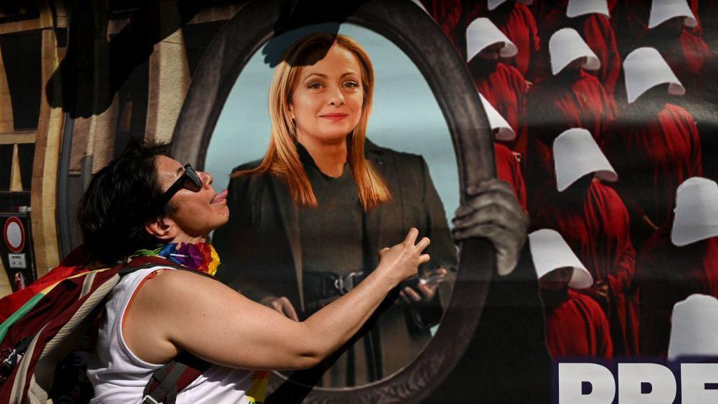 A participant reacts next to a banner depicting Italian Prime Minister Giorgia Meloni during the Pride March to show support for members of the LGBT community, in Milan on June 24, 2023.