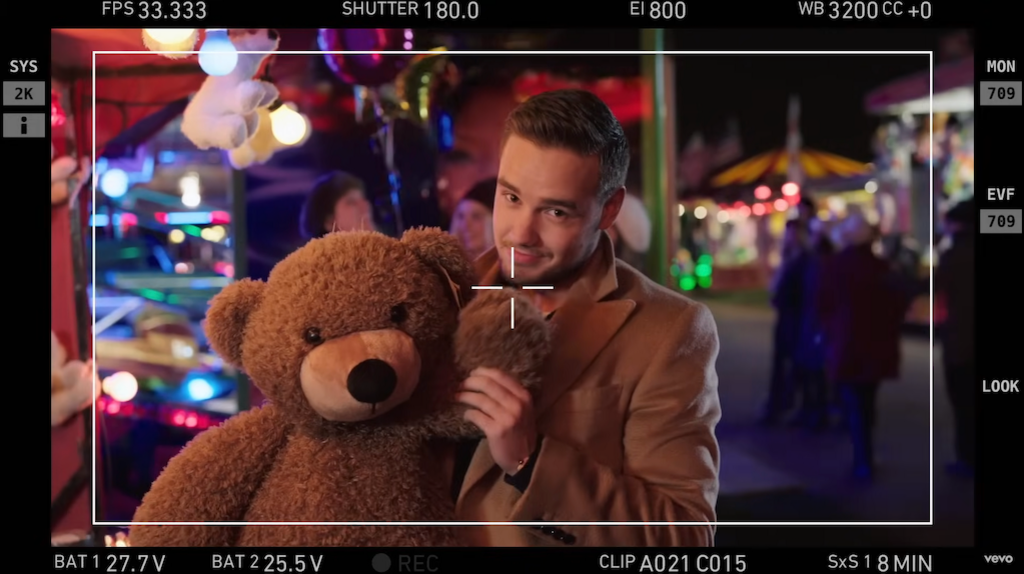 Liam Payne, seen through the viewfinder of a film camera, poses with a teddy bear on the set of the Night Changes video in 2014