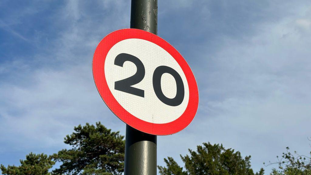 A sign for a 20mph speed limit against a blue sky.