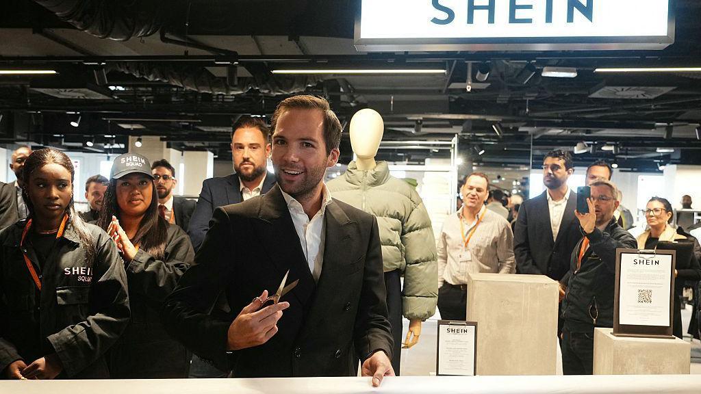 The director of the Bazar de l'Hotel de Ville (BHV) department store Karl-Stephane Cottendin prepares to cut the ribbon at the opening of Asian e-commerce giant Shein's first physical store at the BHV department store in Paris on November 5, 2025