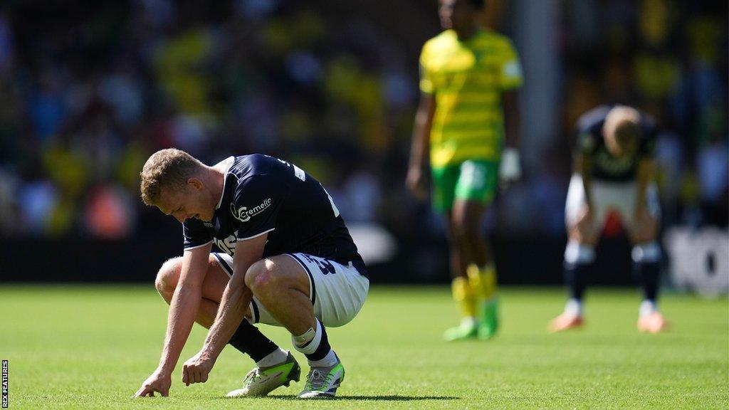 George Saville reacts to Millwall's 3-1 defeat at Norwich City in the Championship by crouching down on the pitch and looking dejected