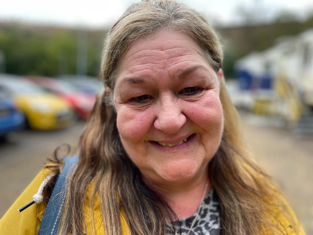 Julie is wearing a yellow coat and has long hair. She is stood outside the mobile lung scanner.