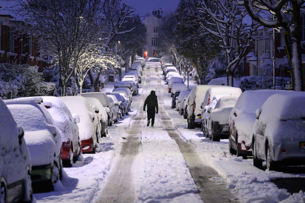 A man walks up a snow-covered road in London