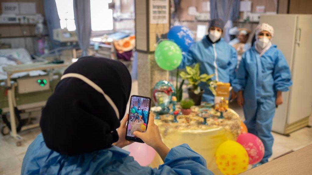 Two Iranian medical personnel wearing protective suits pose for a photograph as they stand next to a Haft-Seen (Seven-S) table, The historical symbol for the Iranian New Year, in a COVID-19 ward in Firoozabadi hospital in Shahr-e-Rey neighborhood in the south of Tehran on the day of Nowruz