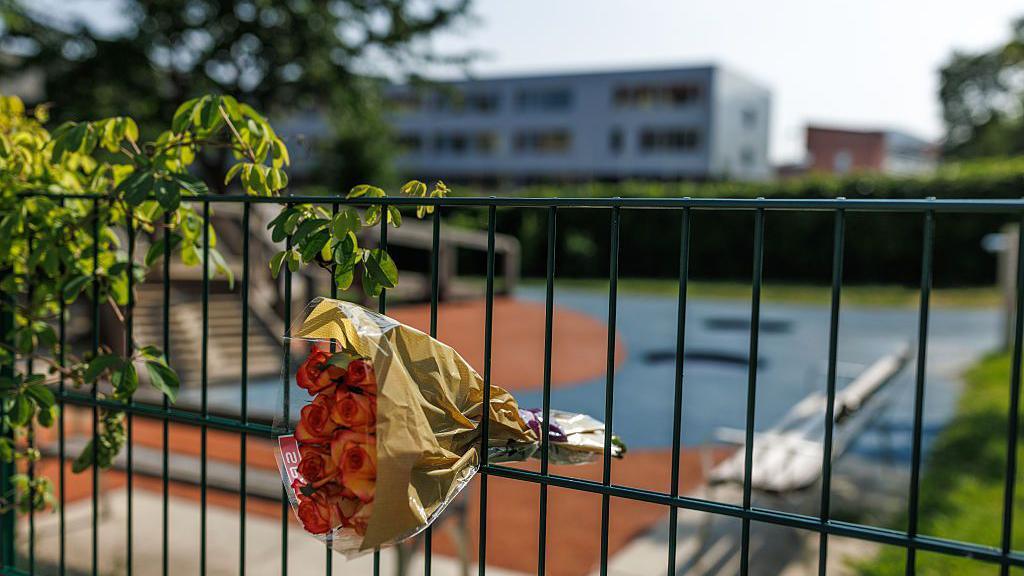 A bouquet of flowers is put into a fence overlooking a school building and grounds