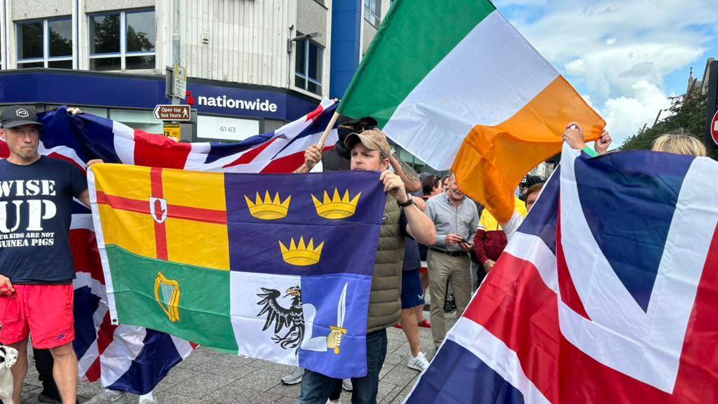 Protesters hold the union jack flag and the irish tri-colour and other flags.