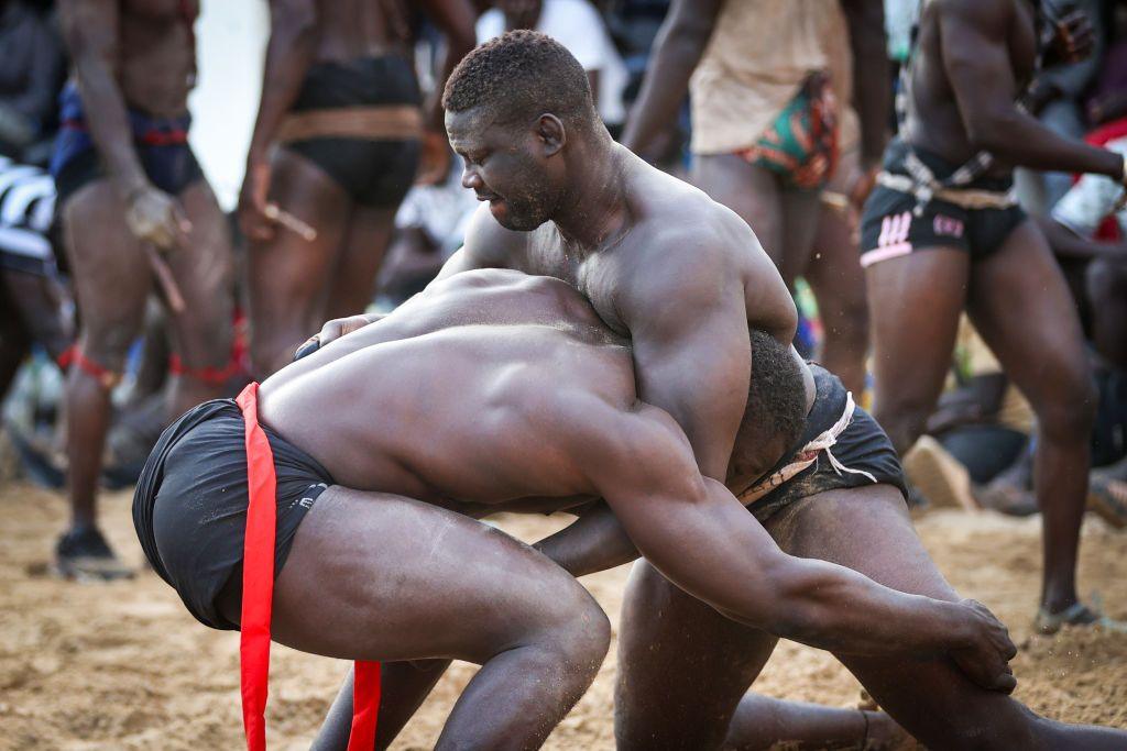 Two muscular men dressed in shorts attempt to pull each other to the ground to win the game.