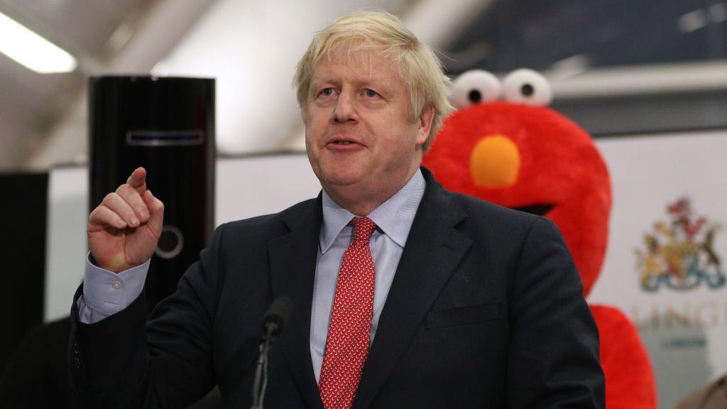 Boris Johnson, standing near a fellow candidate dressed as Elmo, speaks at the vote declaration for his Uxbridge and South Ruislip constituency on December 13, 2019