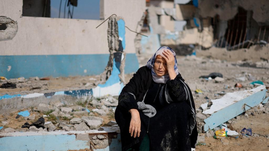 A woman rests next to a damaged building, as Palestinian arrive in Rafah after they were evacuated from Nasser hospital