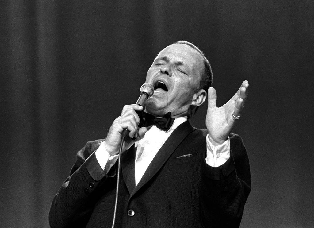 Frank Sinatra, wearing a tux, singing into the microphone with his head leaning back