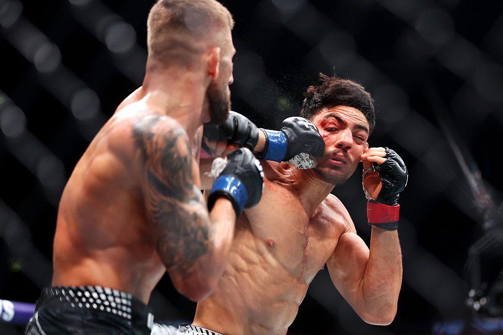 Two mixed martial artists exchange punches inside a caged arena. One fighter lands a powerful strike to his opponent’s face, snapping his head back as sweat and impact freeze mid-action.
