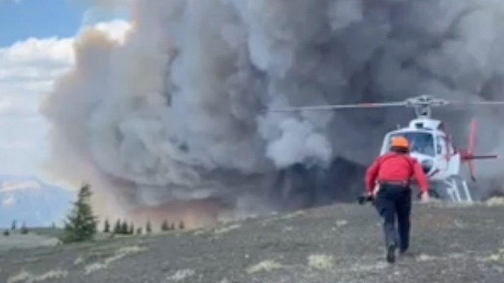 Person running towards a helicopter with smoke in the background