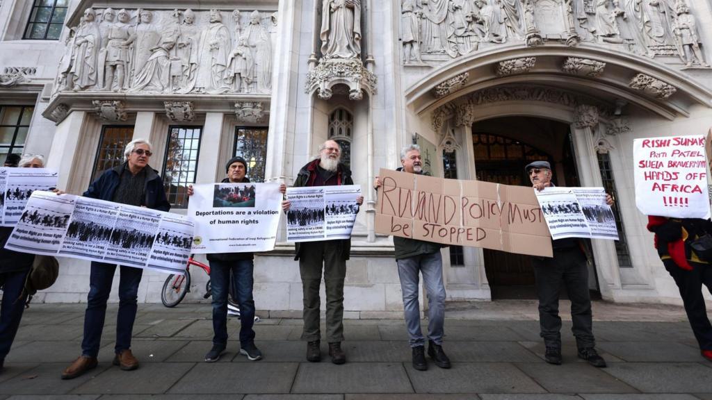 Demonstrators hold placards while protesting against the government's policy of deporting asylum seekers to Rwanda, outside the Supreme Court