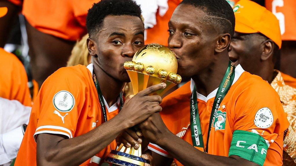 Simon Adingra and Max Gradel celebrate by kissing the trophy after winning the 2023 Africa Cup of Nations final