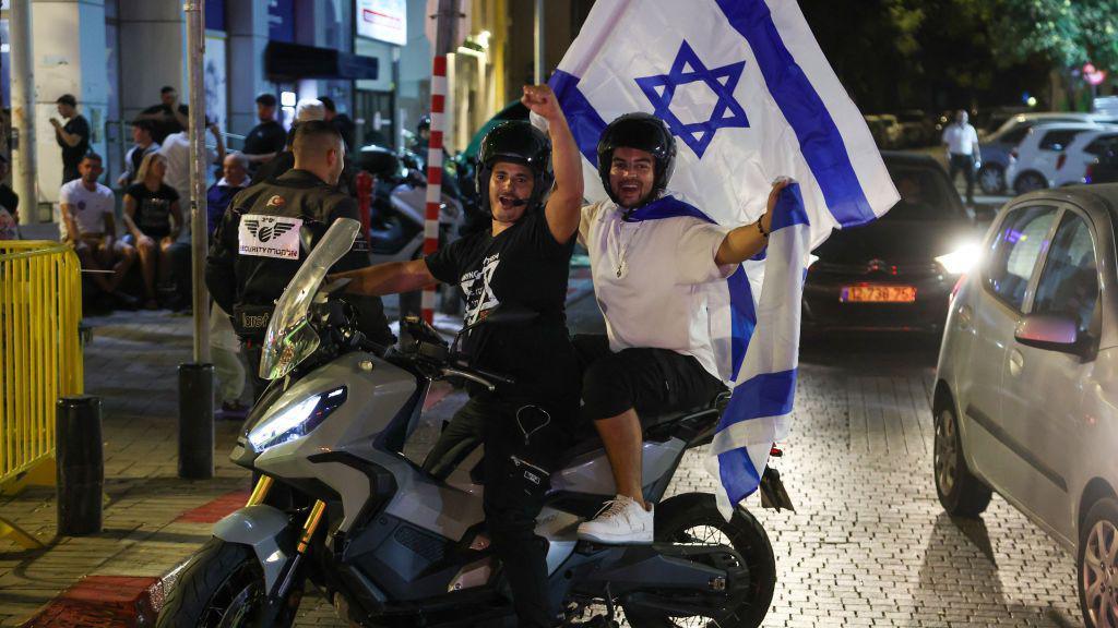 People cheer and wave an Israeli national flags as they celebrate the news of the death of Hamas leader Yahya Sinwar, in the Israeli costal city of Netanya, on October 17, 2024. 