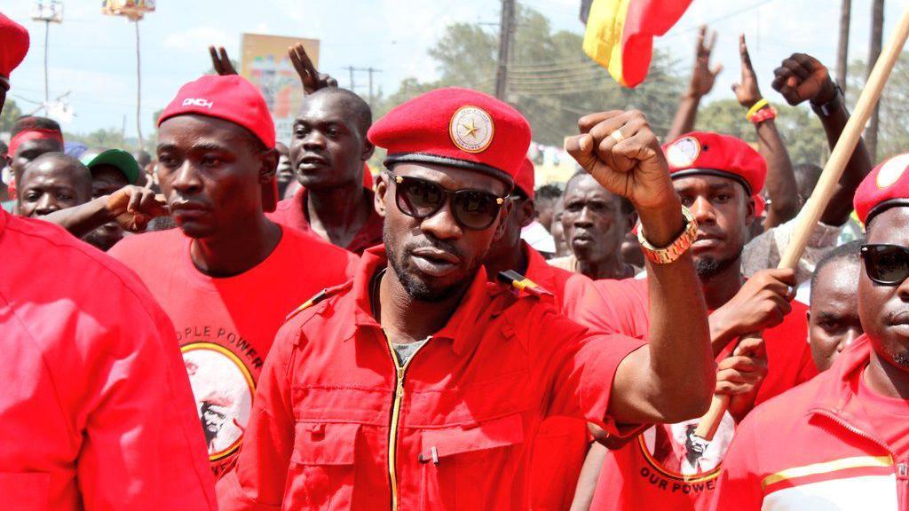 Bobi Wine wearing red overalls at a march with NUP supporters behind him