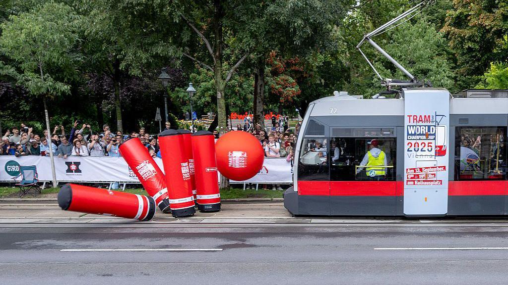 A tram knocking down bowling pins with a huge bowling bowl.
