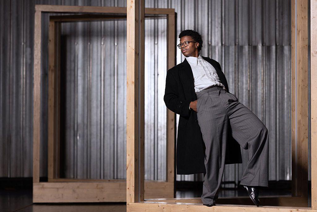 A man dressed in smart clothes leans back and extends one leg.