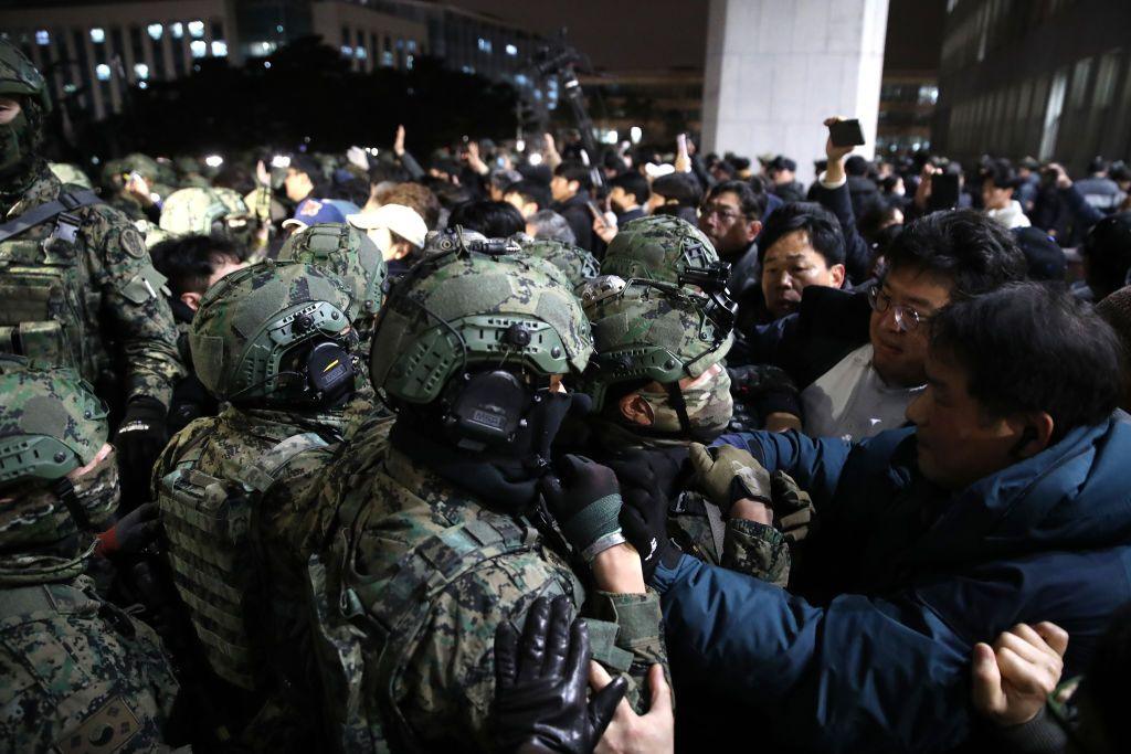 Soldiers wearing helmets and camouflage outfits clash with crowds of civilians during the night