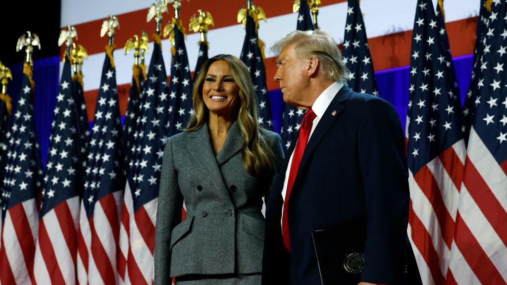 Melania Trump and Donald Trump in West Palm Beach, Florida on the early morning of Nov 6, standing on stage before a row of American flags 