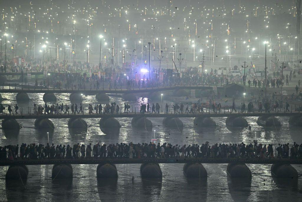 hundreds of people walking across a number of pontoon bridges at night with bright lights in the distance