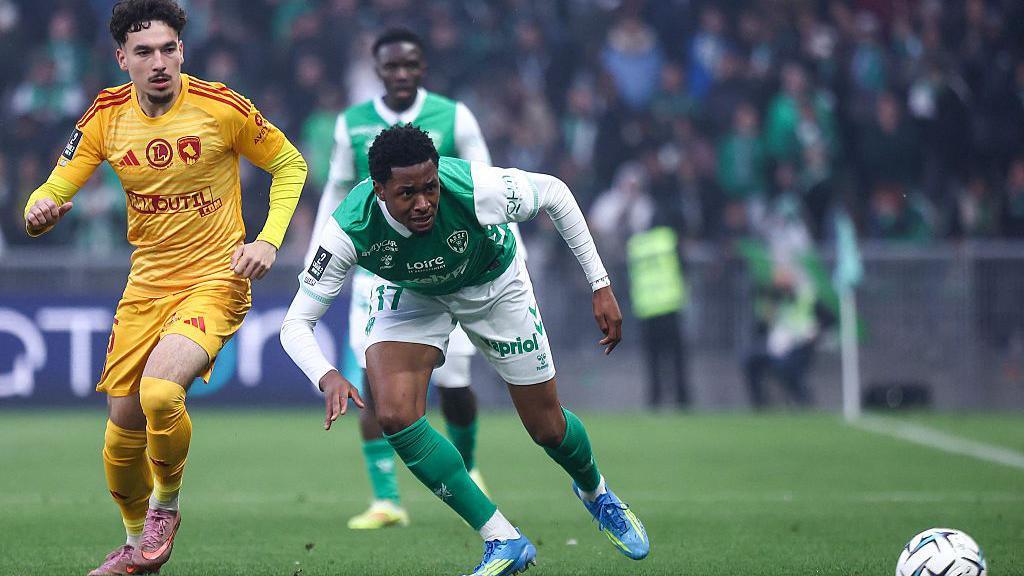 Nolan Galves in action for Rodez. He is wearing a yellow kit is is challenging an opponent who is wearing a green and white shirt