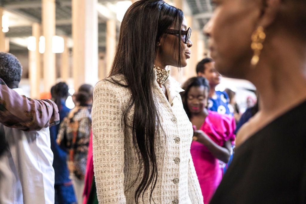 Naomi Campbell (C), looks on during the luxury brand Chanel's fashion show, Metiers d'art, in Dakar on December 06, 2022.She has a cream jacket and is wearing a long wig