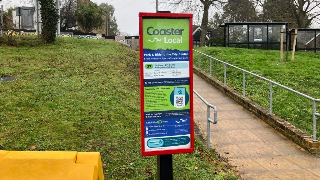 A park and ride bus board. There is green grass in the background.