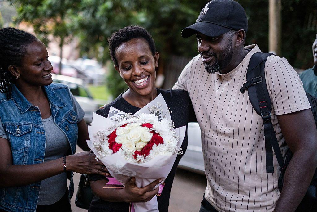 A smiling woman is given a bouquet of flowers by people who are smiling and embracing her.
