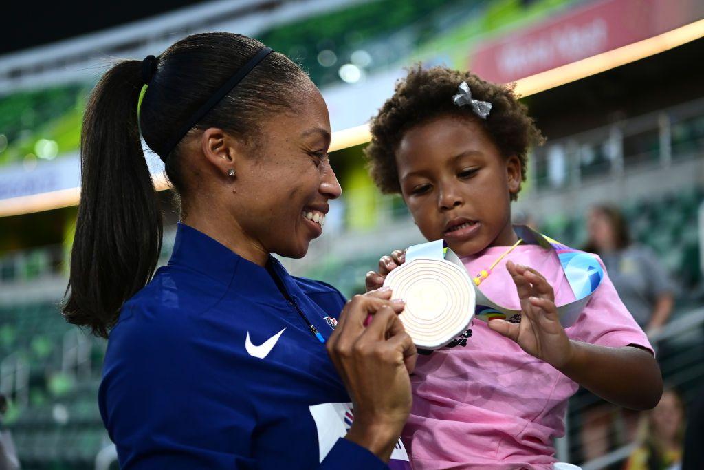 Image of athlete wearing a Nike top and holding her daughter whilst showing her a medal.