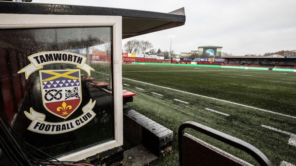 General view across the pitch at The Lamb, home of Tamworth FC with the dugout in the foreground. The club crest is on the side window of the dugout.